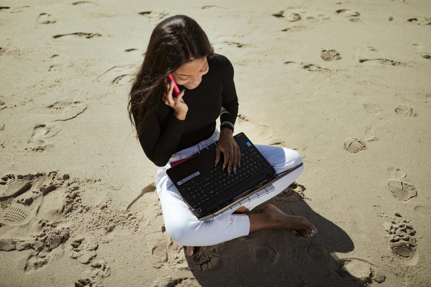Woman working remotely on a beach, using a laptop and talking on the phone. on The Anywhere Office