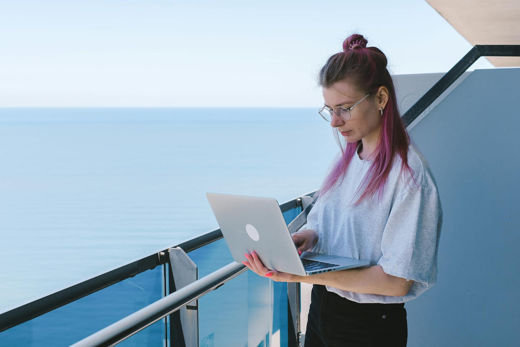 A young woman works remotely on her laptop by the sea on a sunny day, embodying the digital nomad lifestyle. on The Anywhere Office