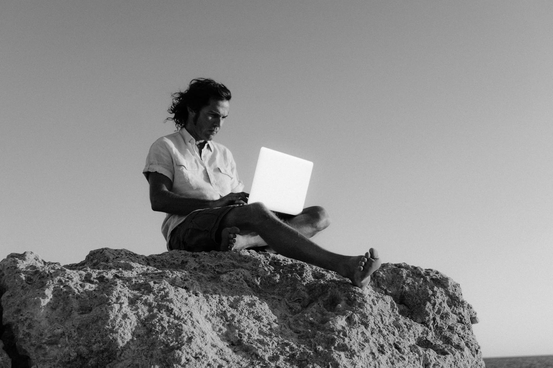 A digital nomad works on a laptop while sitting on a rocky cliff, embodying remote work lifestyle. on The Anywhere Office