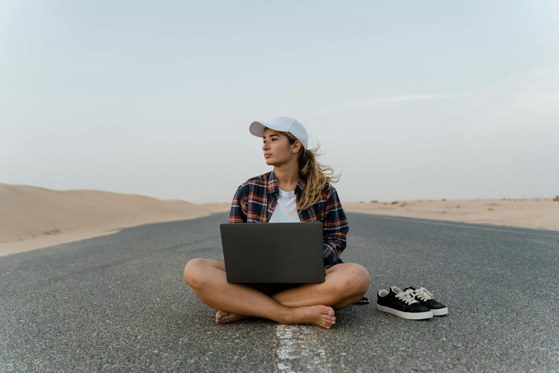 A woman works remotely on a laptop while sitting barefoot on a desert road. on The Anywhere Office
