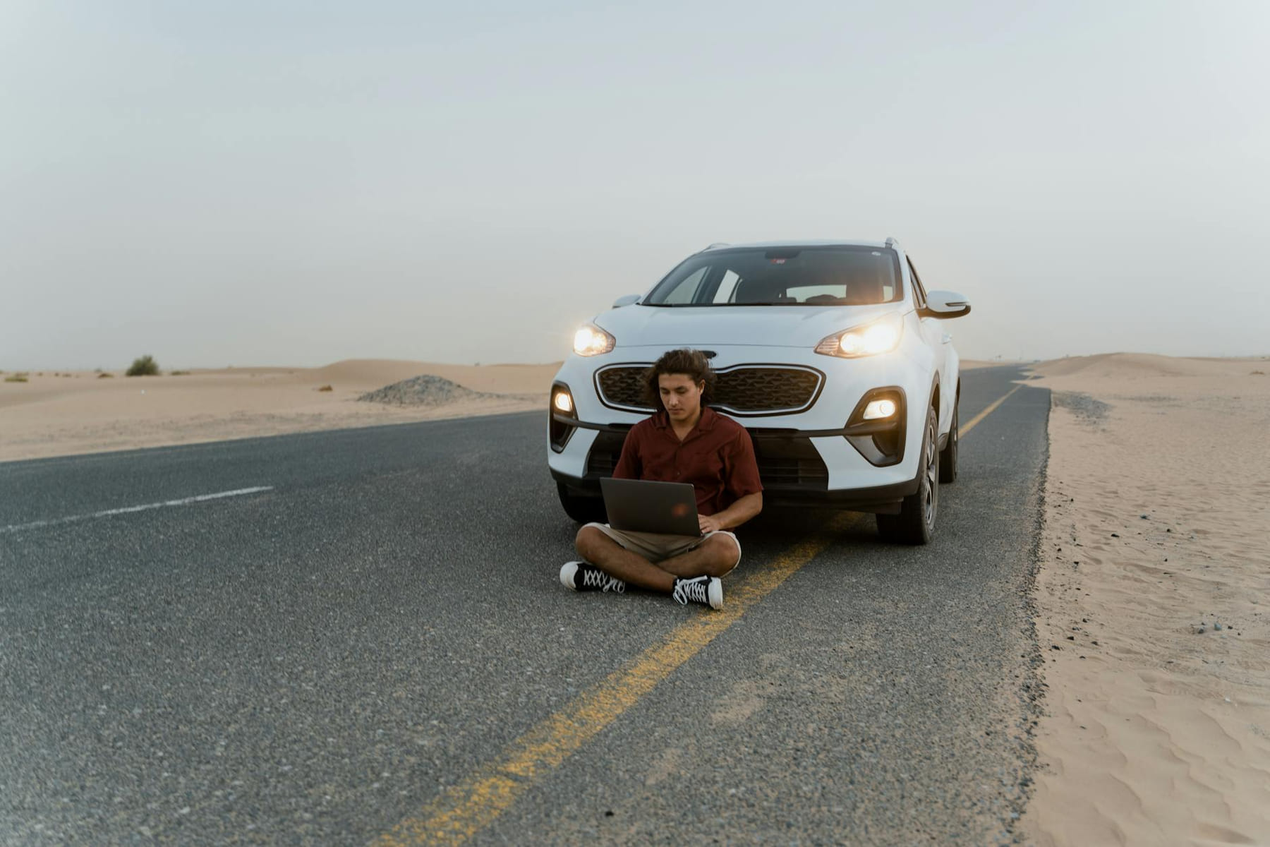 A man working on a laptop beside a car on a desert road, symbolizing remote work freedom. on The Anywhere Office