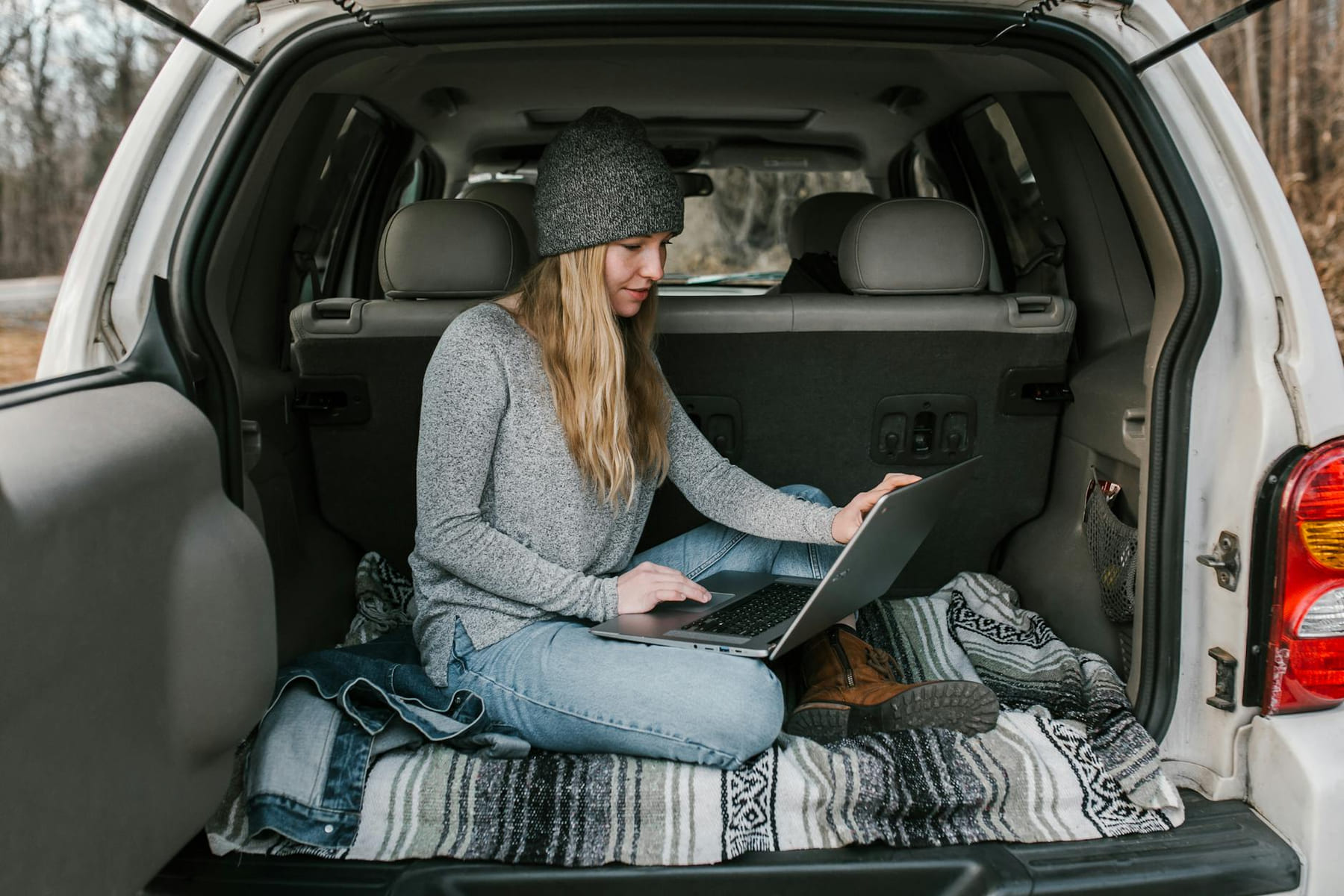 A young woman working remotely on a laptop from the cozy trunk of a vehicle. on The Anywhere Office