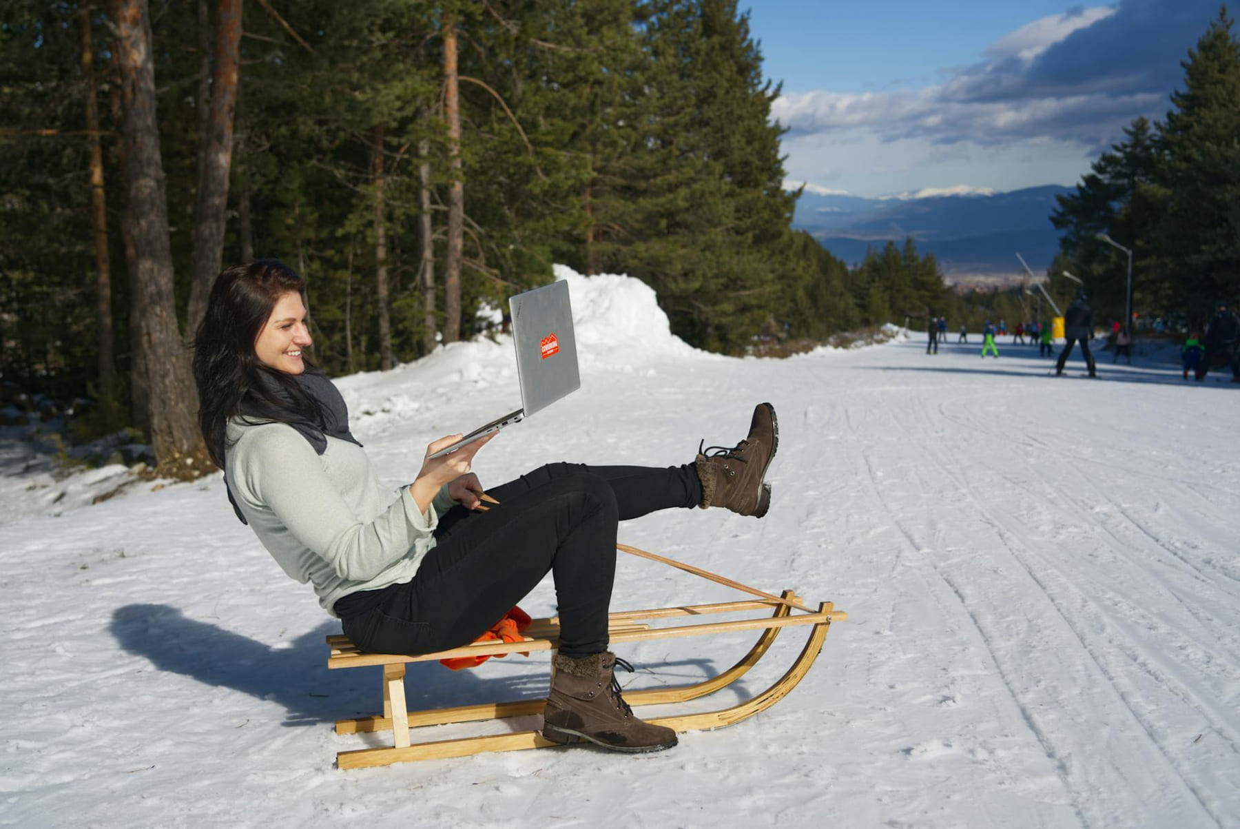 Woman on sled using laptop in a ski resort, embracing the digital nomad lifestyle. on The Anywhere Office