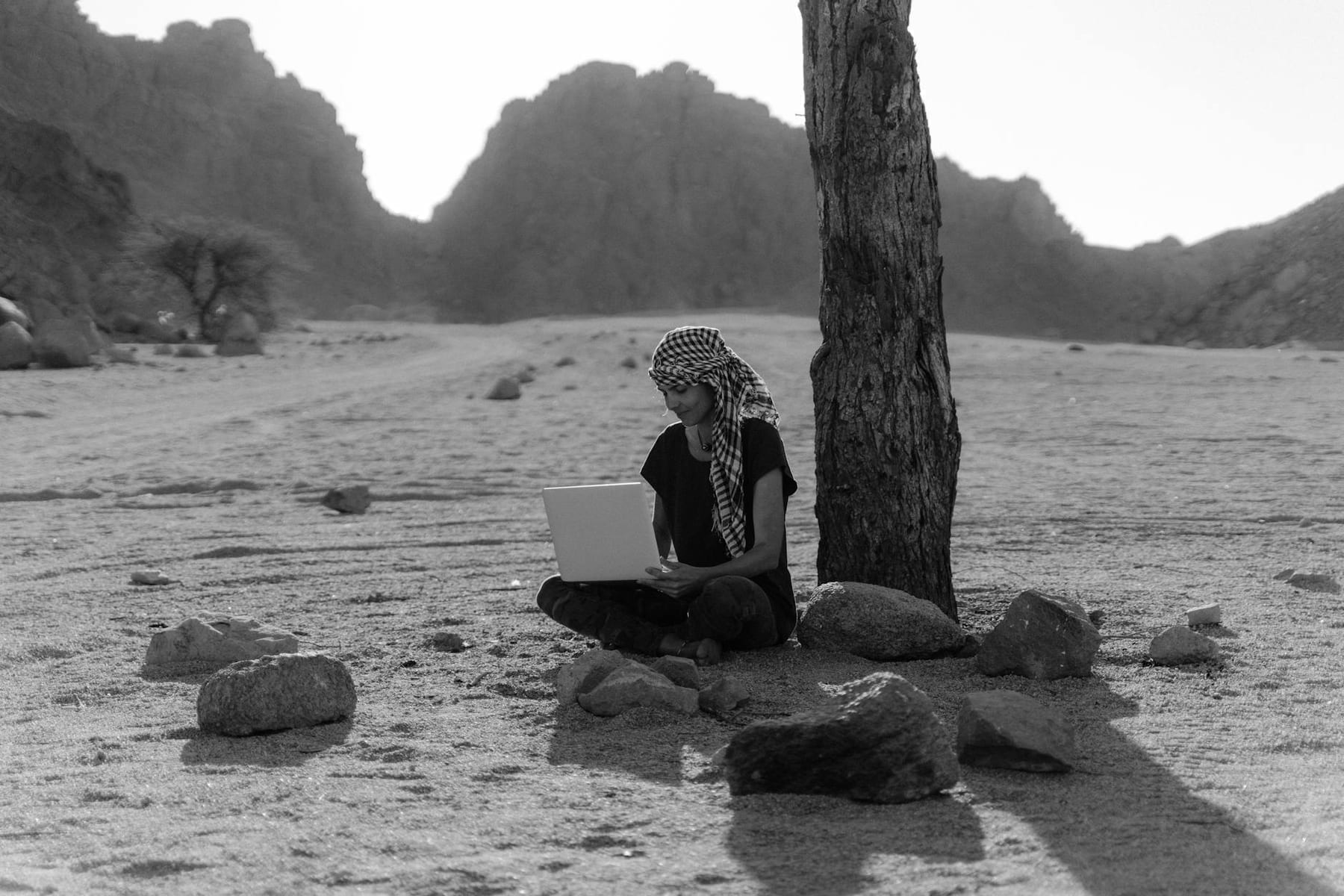 A woman working remotely on a laptop under a tree in a desert landscape. on The Anywhere Office