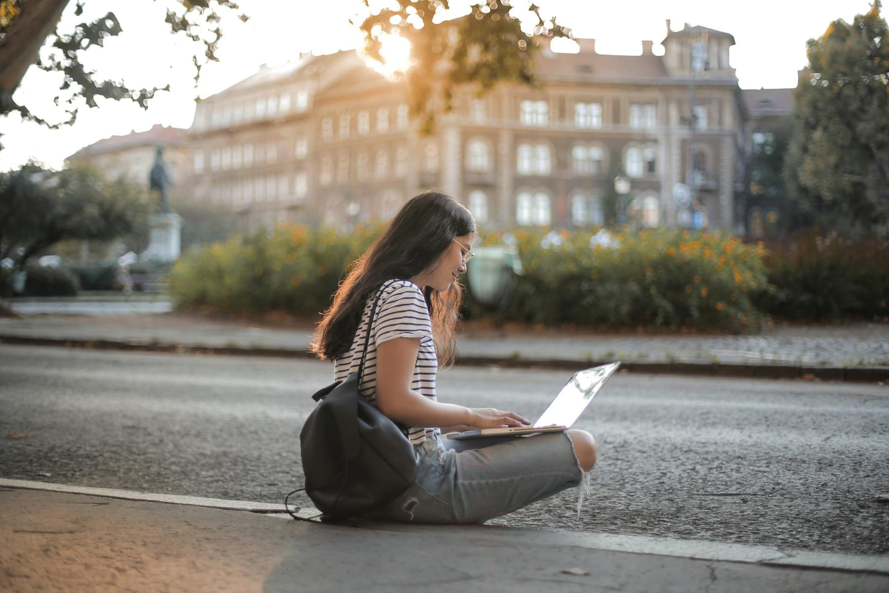 Young woman using laptop outdoors in urban area, showcasing remote work lifestyle. on The Anywhere Office