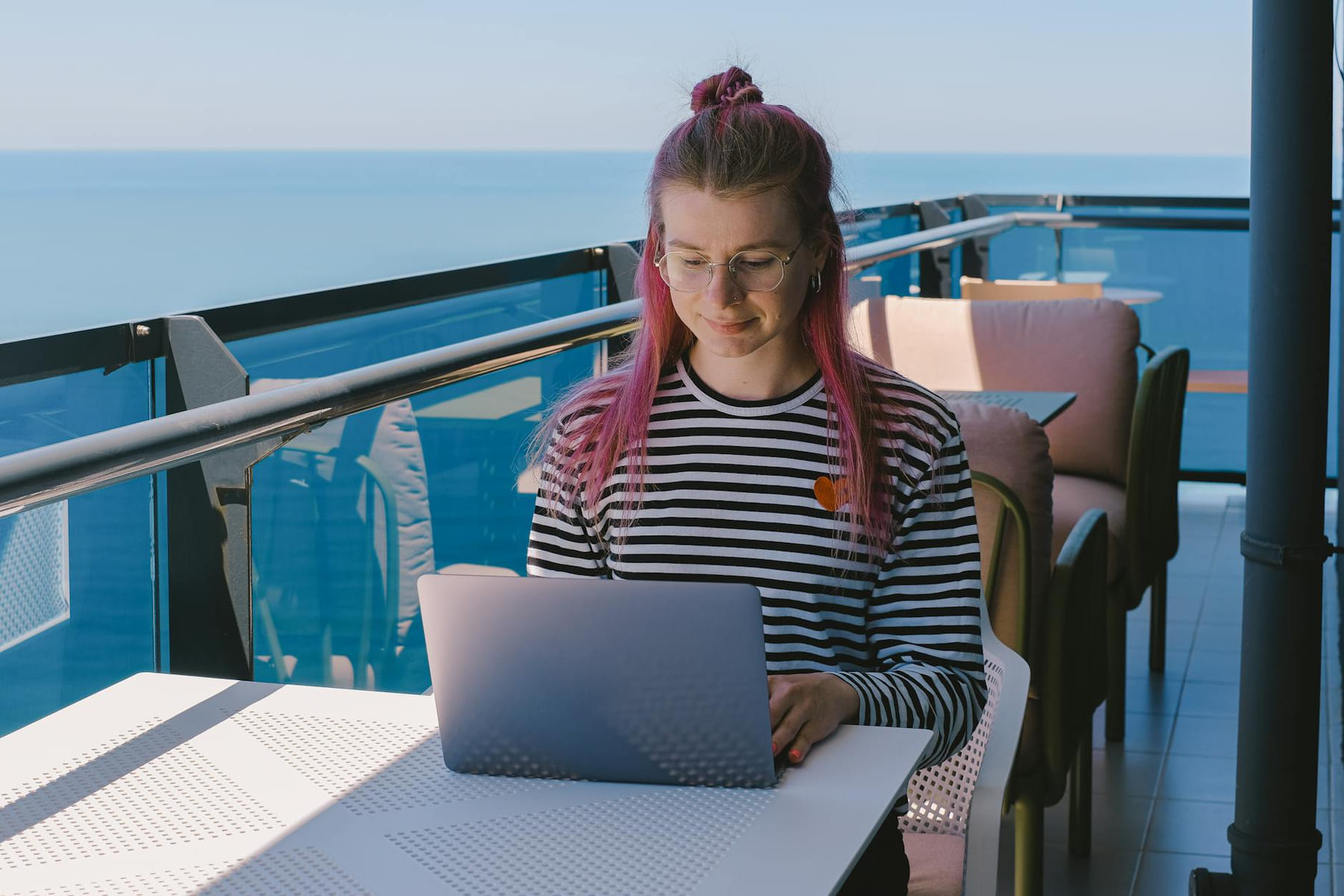 Young woman freelancing with a laptop on a sunny oceanfront balcony, embracing remote work lifestyle. on The Anywhere Office