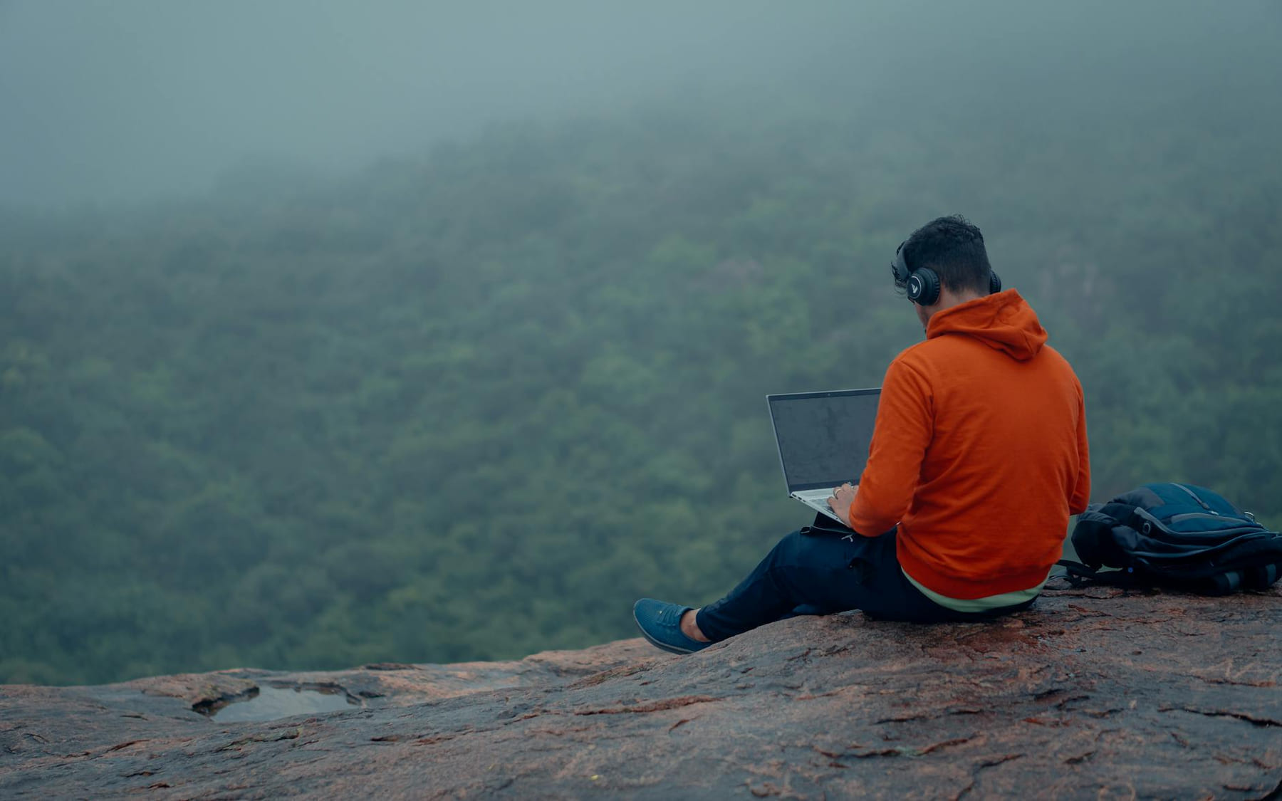 Man in hoodie working on laptop in misty forest, Bengaluru. Modern remote work. on The Anywhere Office